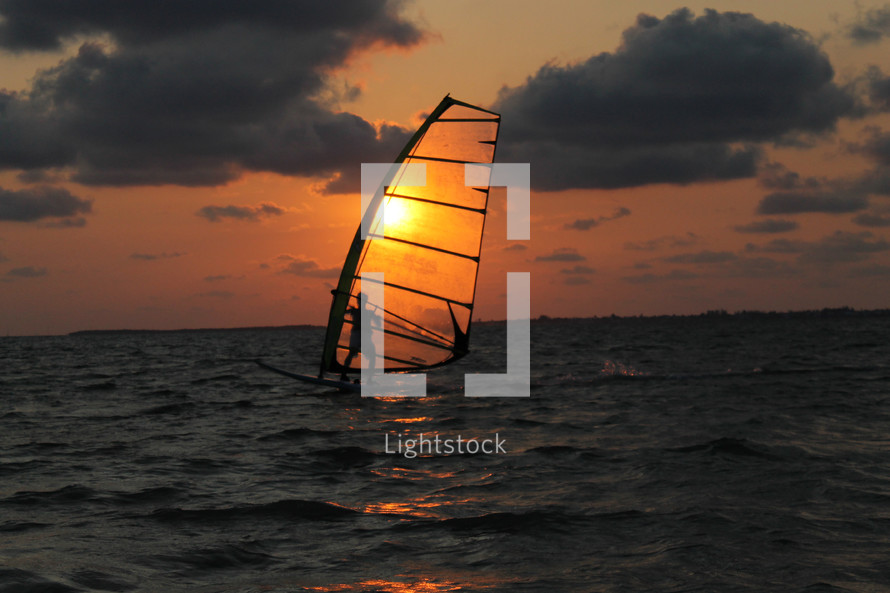 Sunset behind a sail surfer on the ocean water.