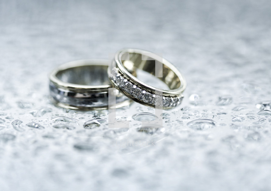 Close up of wedding rings on top of glass table with little puddles from rain drops.