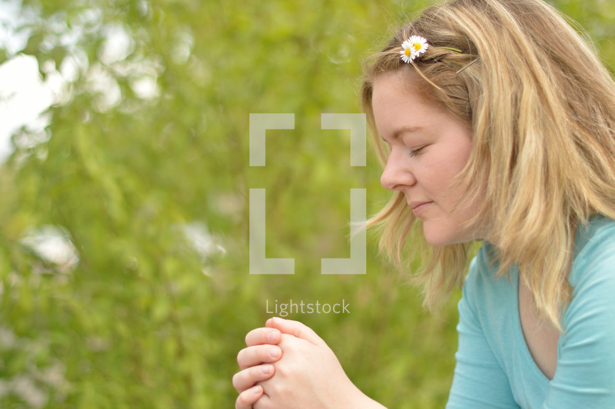 Young blonde woman praying outdoors. 