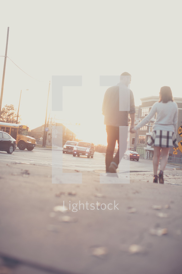 A couple walks along the street holding hands.