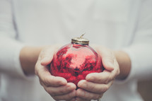 Hands holding a red Christmas ornament