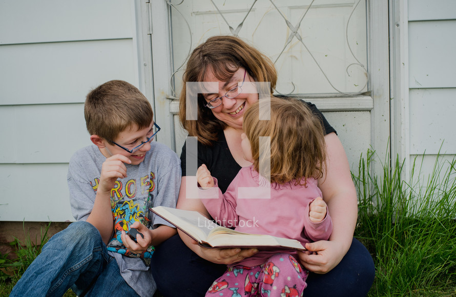 a mother reading a Bible to her children outdoors 
