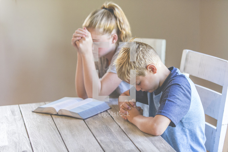 a brother and sister reading a Bible and praying 