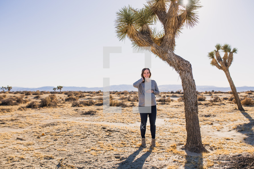 a woman standing in a desert under a tree