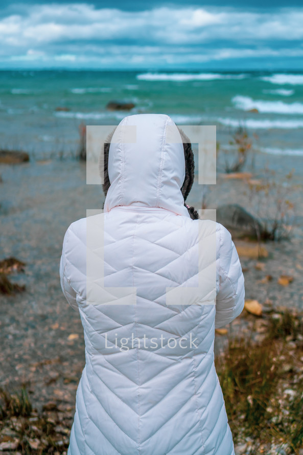 a woman in a coat looking out at the ocean 