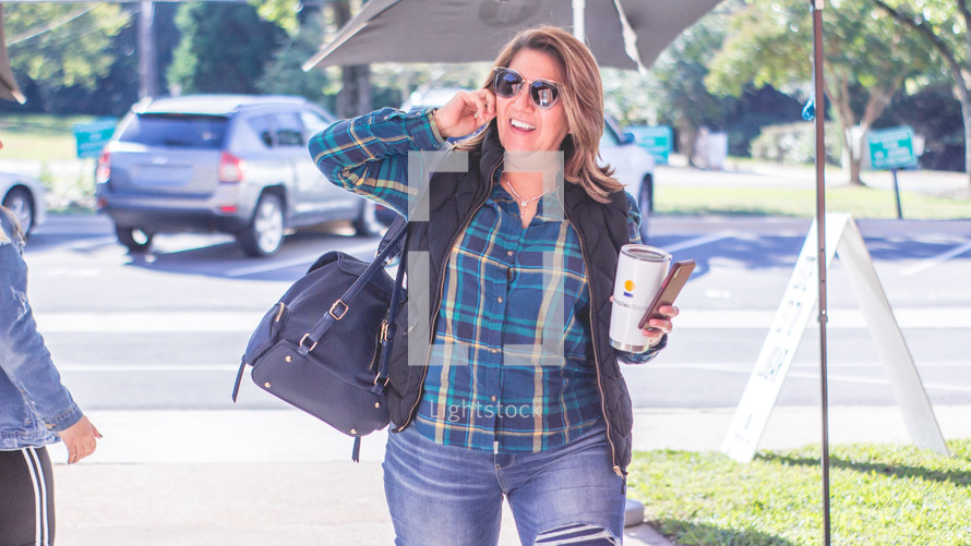 a woman taking on a cellphone and carrying a to go coffee cup 