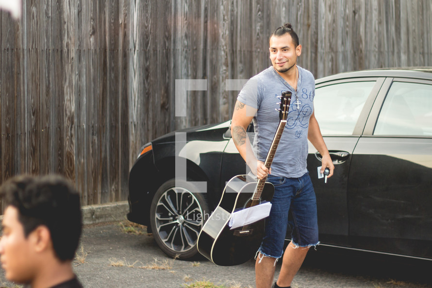 man stepping out of his car holding a guitar 