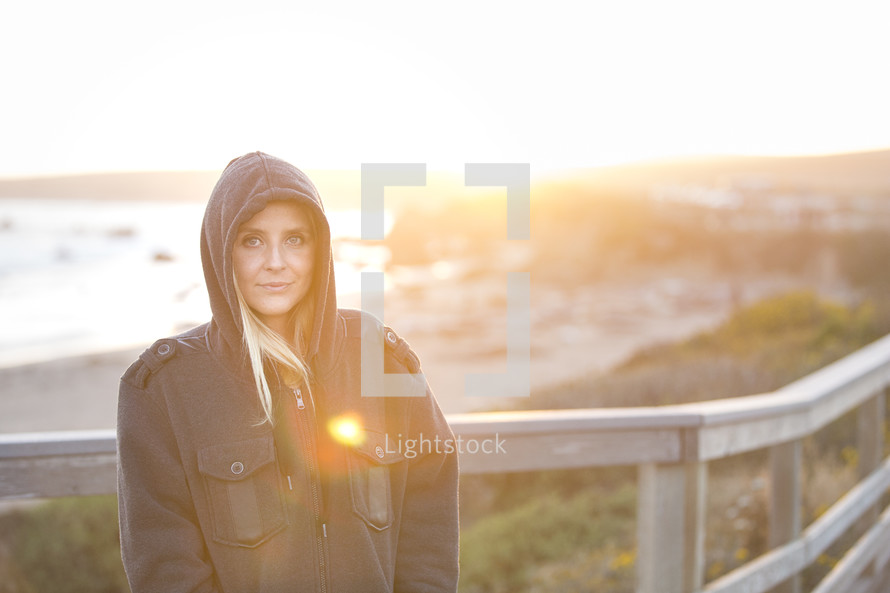 portrait of a woman in a hoodie standing on a shore 