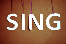 Letters spelling the word, "sing," suspended from strings.