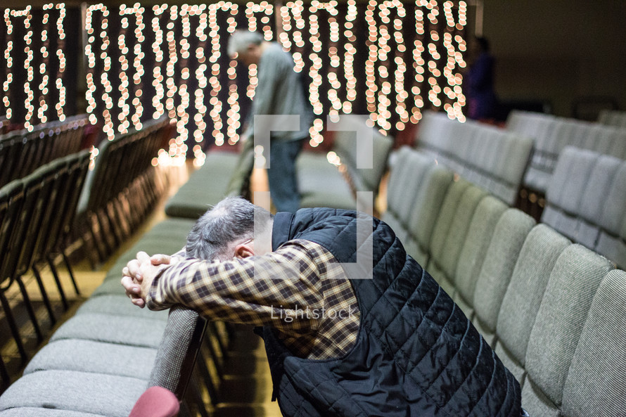 man praying over the back of a chair at church 