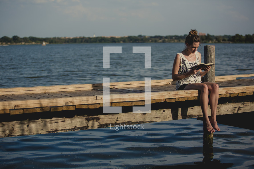 girl reading a Bible with her feet in the water 