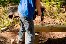 a boy drilling a hole in a board outdoors on a farm 