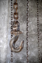A large hook and chains. 
hook, chains, chain, industrial, hoist, hang, building, hang up, caught, snag, lock, raise, raising, pull, pulling, up, down, hike up, hoisting, lift, lifting, wind, winding, bound, trussed, tied, metal, ferric, iron 