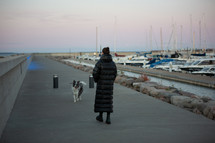 Woman in heavy coat walking her dog by boats