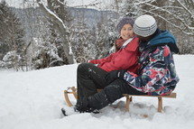 smiling couple sitting together on a sled in the snow