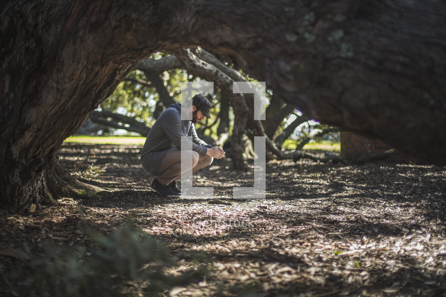 a man squatting under trees in prayer to God 