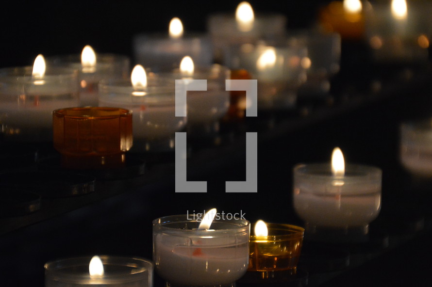 many lit candles in a dark church. 
candle, lit, flame, fire, burning, candles, flames, kindled, light, lighted, blaze, blazing, burning, burn, many, much, lot, dark, lighten, brighten, bright, illuminate, illumine, shine, shining, see, seeing, show, showing, symbol, symbolic, symbolize, symbolizing, believe, believers, wax, church, pray, prayer, votive, darkness, burnt, donation, donate, ceremony, offering, offer, yellow, white, orange, row, line, lines, commemorate, remember, recall, remembrance, memory, memento, think of, sign, creed, unlit, rows