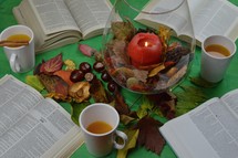 apple cider, open Bible, candle, and fall leaves on a green background 