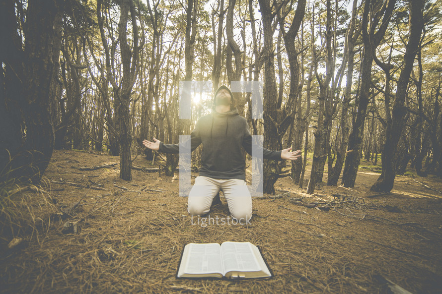 a man kneeling in front of a Bible in the forest praising God 