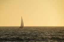 little sailboat sailing on the wide ocean in the yellow light of sundown. 
