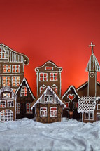home made gingerbread village in front of red background on white snowlike velvet as advent decoration