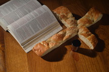 open Bible, bread in the shape of a cross, and cup of communion wine 