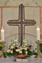 Cross, candle sticks and a flower arrangement on an altar. 