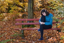a woman sitting on a bench in a park in fall lost in thoughts