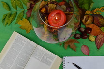 notebook, pen, open Bible, candle, and fall leaves on a green background 