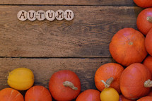 Pumpkins on wooden planks with pieces of wood spelling the word AUTUMN. 