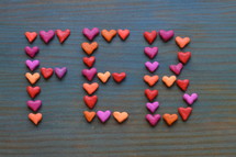 The word FEB for February written with many little colorful clay hearts on cyan wooden background 