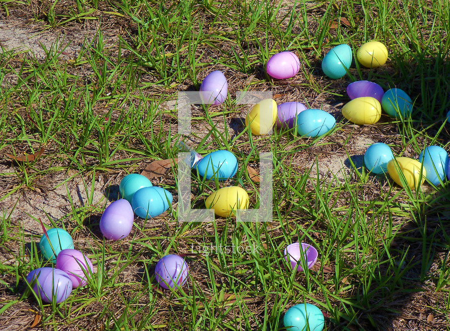 A green field with pastel colored Easter eggs including blue, purple, aquamarine blue, green and yellow greet kids going on an Easter egg hunt at a local church ground during the Easter holiday. 