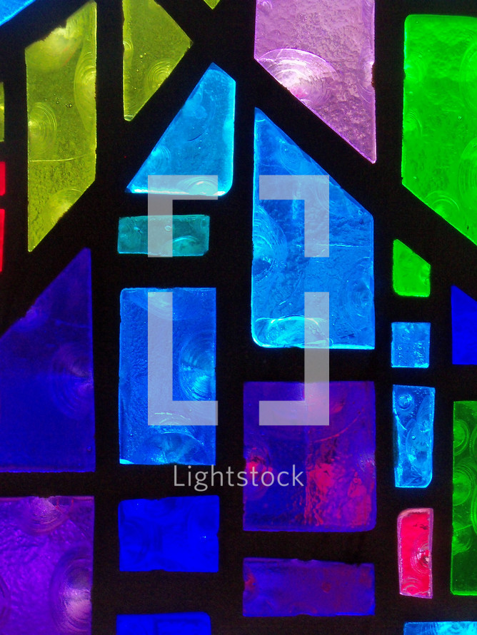 A close-up view of a stained glass window panel with vivid shades of blue, green and purple colors adorning a church sanctuary. 