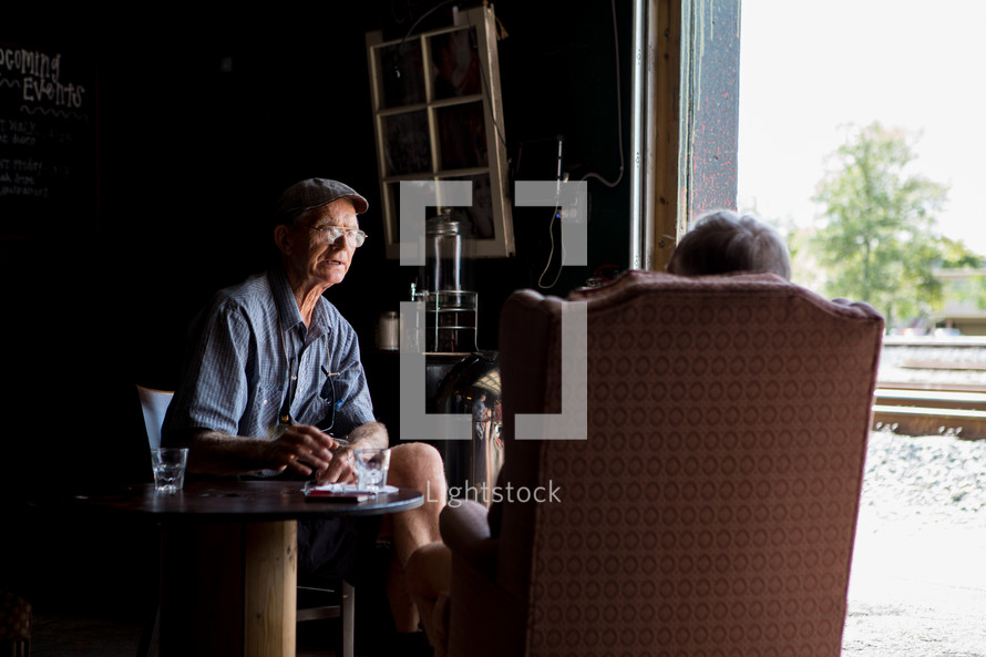 elderly men talking while sitting near a window 
