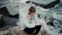 woman sitting on a rock with sea water splashing up 