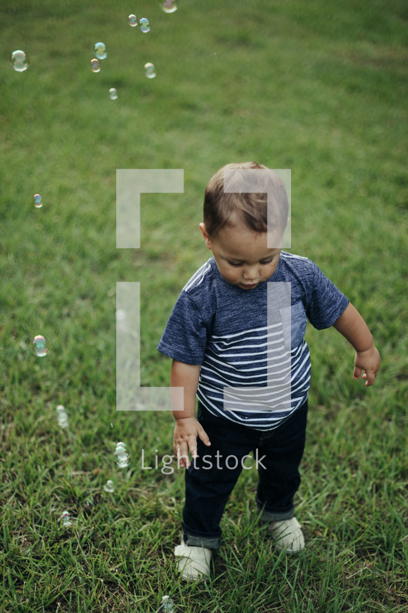 a toddler boy chasing bubbles in the grass 