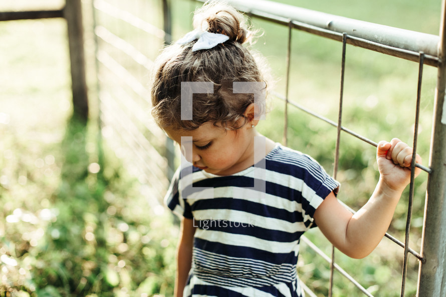 a toddler girl hanging onto a fence 