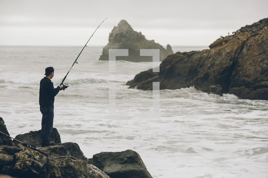 man standing on rocks fishing in the ocean 