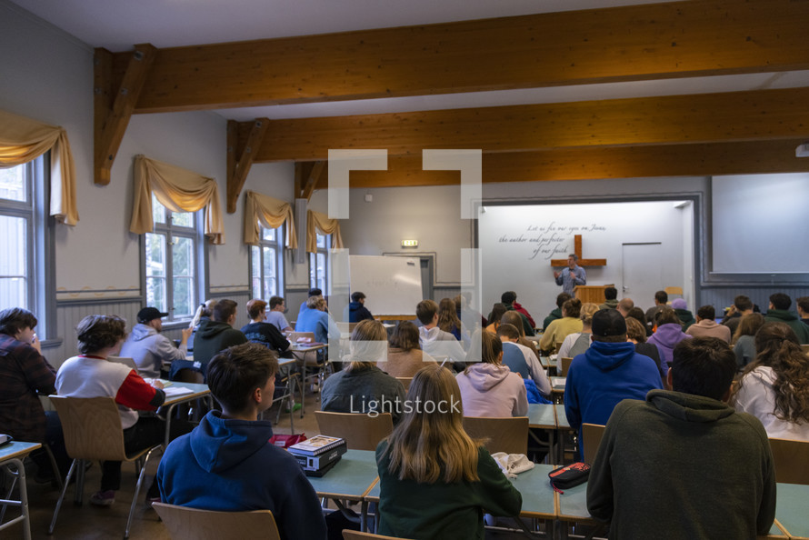 People sitting at tables in a chapel, classroom while someone teaches from the front