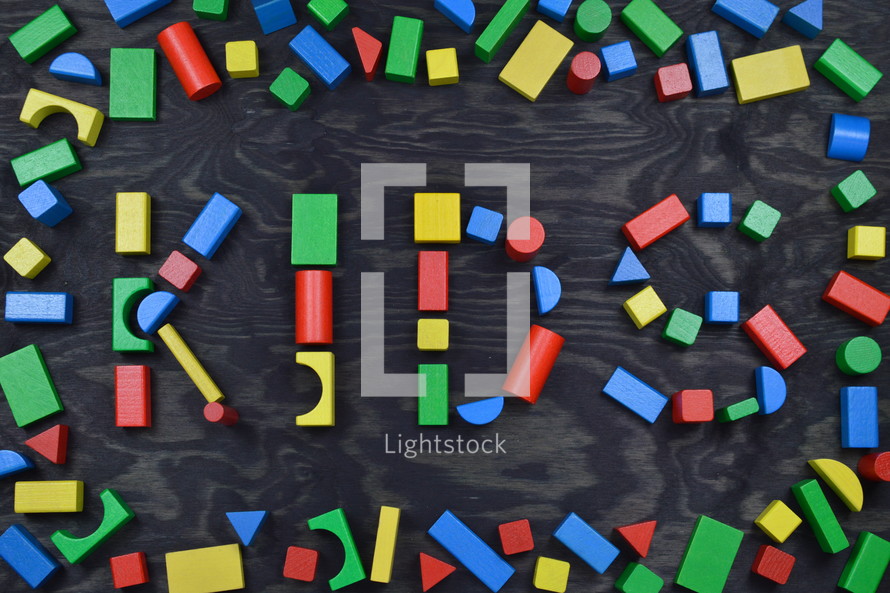 the word KIDS out of colorful wooden toy blocks on black wooden background with frame out of toy blocks