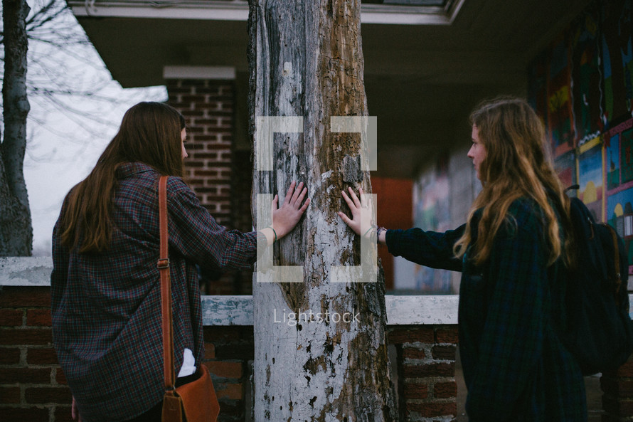 two young women with their hands on an old post 