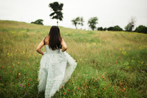 woman in a white dress walking through a meadow of wildflowers 
