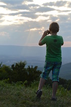 a young boy taking a picture on a mountaintop 