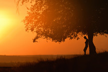 silhouette of a man standing under a tree at sunset 