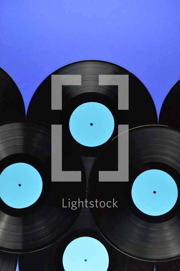 pile of old black vinyl records with blank cyan labels on blue background with copy space above