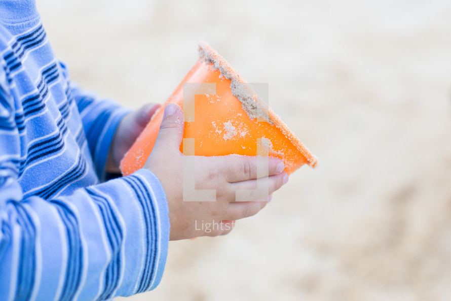a child's hands holding a sand bucket 