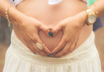 a pregnant woman making a heart shape with her hands over her belly 