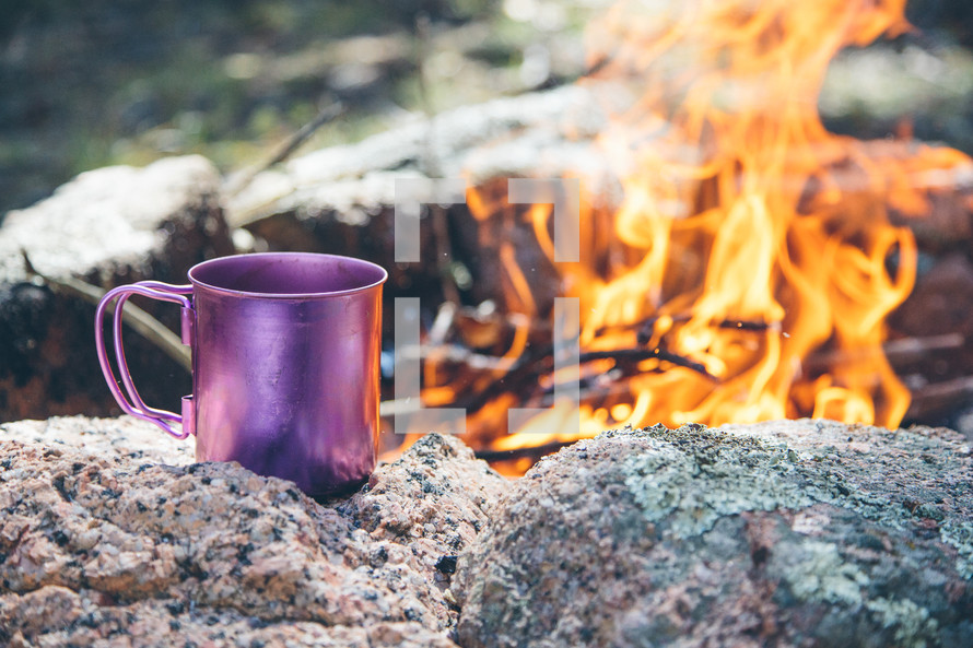 a coffee mug next to a camp fire 