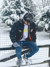 a man sitting on a fence in the snow 