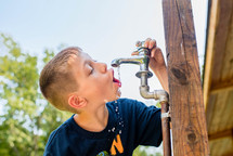 a boy drinking from an outdoor spigot 